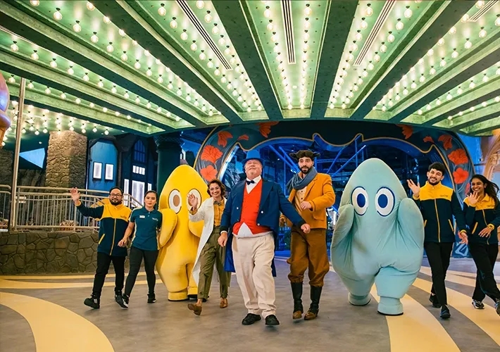 Cheerful mascots and staff welcome guests at a colorful indoor theme park venue .